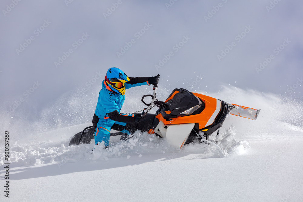 the guy turns a snowmobile in a mountain valley on the background of the clear snow and sky, leaving behind a trail of splashes. bright snow bike and suit without brands. Boondocker sports snowmobile