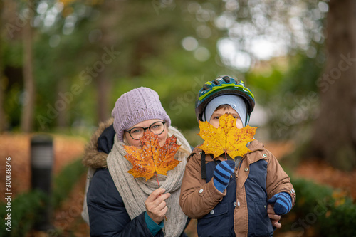 mother and son in autumn park  covering faces with autumn leaves  fall background  creative concept