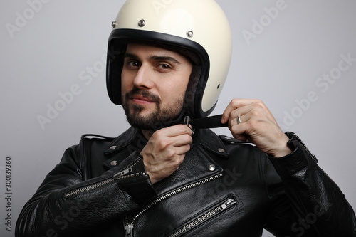 Close up portrait of young and handsome biker looking at the camera and fasten up his helmet.