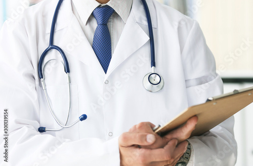 Close-up of clipboard with blank paper in medical doctor hand. Male doctor listens to the patient holding a clipboard with documents for hospitalization.
