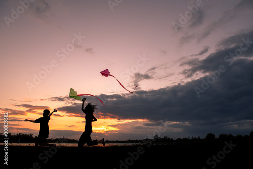 The little boy was playing kite at the park in the evening with sunset and silhouette.