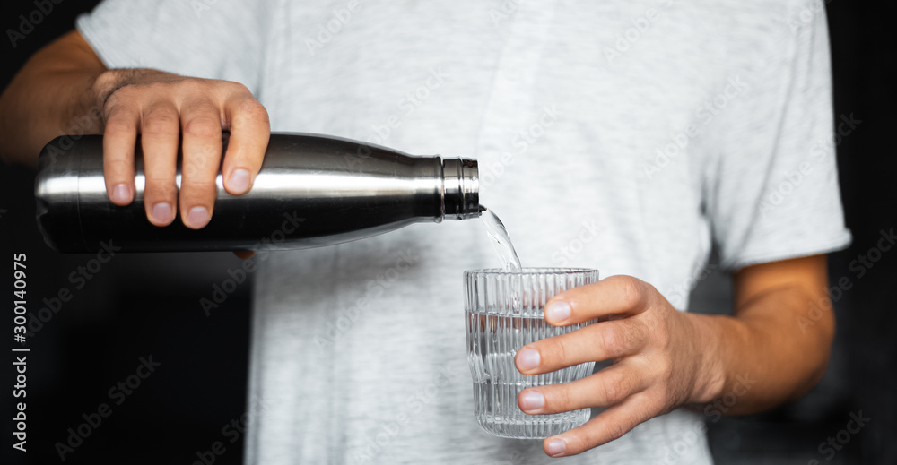 Naklejka premium Male hands pours water into a glass from steel thermo eco bottle.