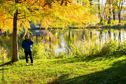 Man standing in the park during the morning of an autumn season day. He is holding the coffee mug for the morning drink.