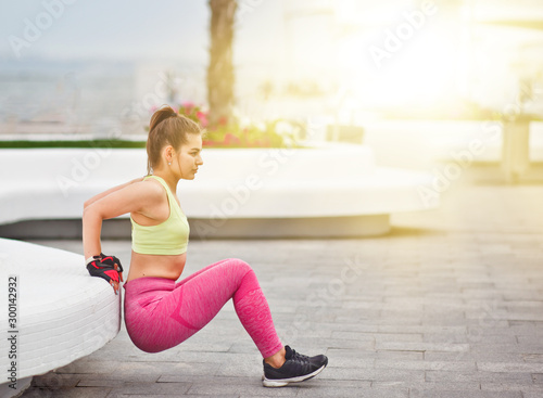 Young attractive woman doing exercise rear pushups for triceps. outdoors in urban environment