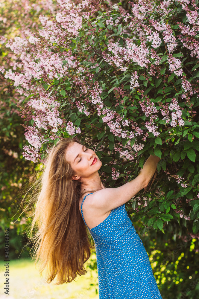 Portrait of smiling girl with blond hair and closed eyes and blue dress among lilac Portrait of smiling girl with blond hair and closed eyes and blue dress among lilac