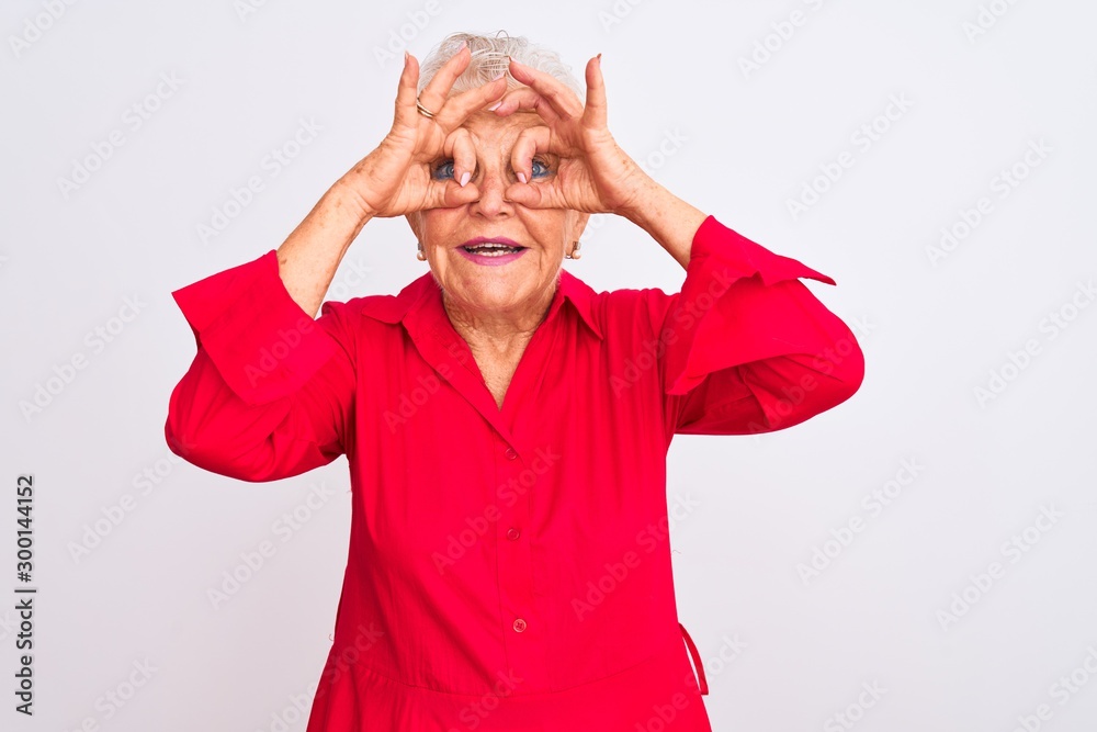 Senior grey-haired woman wearing red casual shirt standing over isolated white background doing ok gesture like binoculars sticking tongue out, eyes looking through fingers. Crazy expression. Senior grey-haired woman wearing red casual shirt standing over isolated white background doing ok gesture like binoculars sticking tongue out, eyes looking through fingers. Crazy expression.