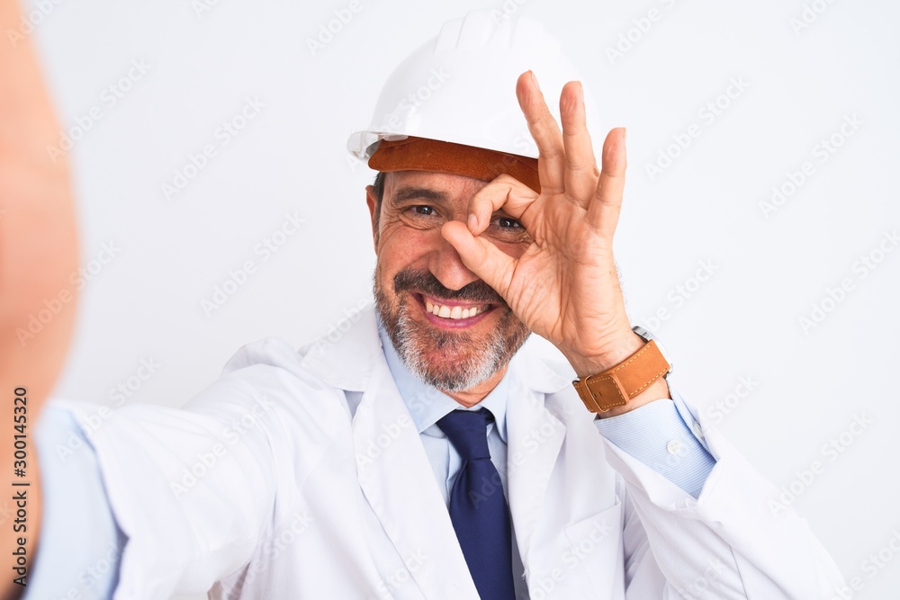 Middle age engineer man wearing helmet make selfie over isolated white background with happy face smiling doing ok sign with hand on eye looking through fingers Middle age engineer man wearing helmet make selfie over isolated white background with happy face smiling doing ok sign with hand on eye looking through fingers