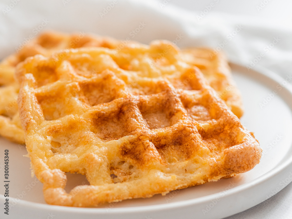 Perfect savory keto waffles. Two ingredients chaffles on plate over white marble background. Eggs and parmesan cheese low carb waffles. Extreme close up view. Perfect savory keto waffles. Two ingredients chaffles on plate over white marble background. Eggs and parmesan cheese low carb waffles. Extreme close up view.