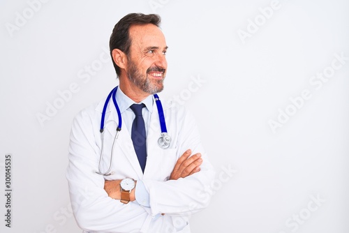 Middle age doctor man wearing coat and stethoscope standing over isolated white background smiling looking to the side and staring away thinking. © Krakenimages.com