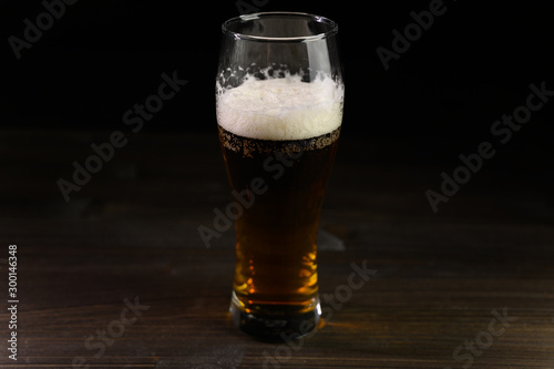 Photo of beer in a glass. Thick foam and a nice color drink on a black background.