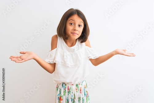Young beautiful child girl wearing casual dress standing over isolated white background clueless and confused expression with arms and hands raised. Doubt concept.