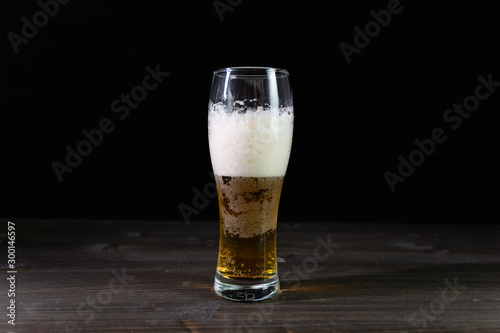 Photo of beer in a glass. Thick foam and a nice color drink on a black background.