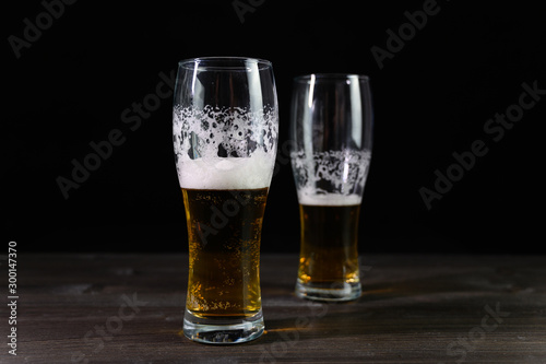 Photo of beer in two glasses. Thick foam and a nice color drink on a black background.