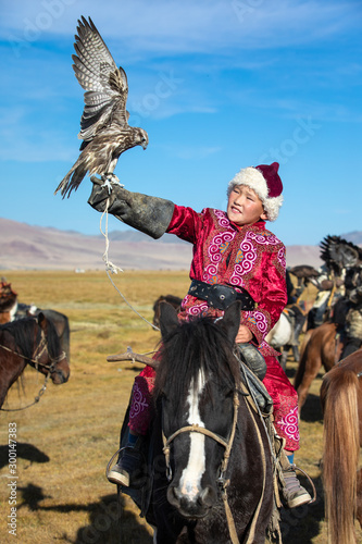 Young Mongolian boy in traditional Mongolian dress holding his falcon on horseback. Young children start training with falcons prior to working with golden eagles. Ulgii, Mongolia. photo