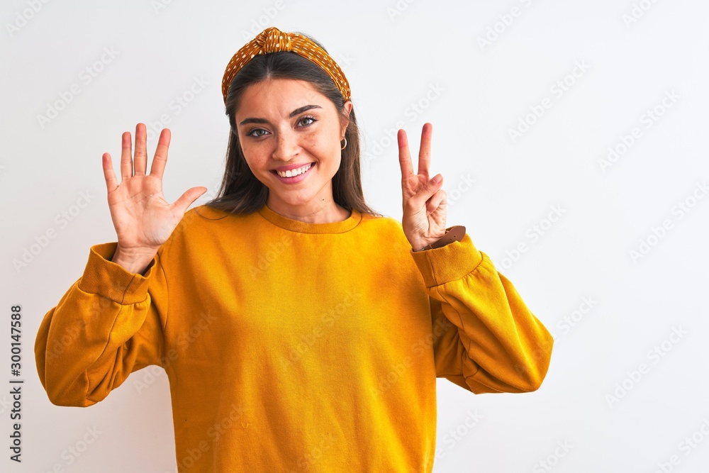 Young beautiful woman wearing yellow sweater and diadem over isolated white background showing and pointing up with fingers number seven while smiling confident and happy.