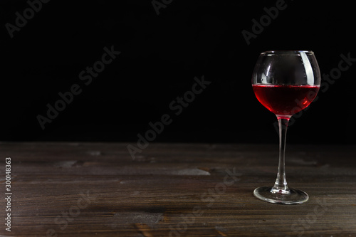 Photo of red wine in a glass on a wooden table. Nice color drink on a black background.
