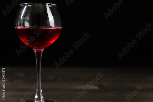 Photo of red wine in a glass on a wooden table. Nice color drink on a black background.