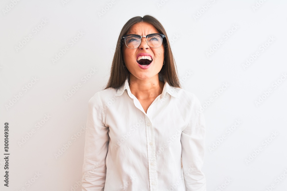 Young beautiful businesswoman wearing glasses standing over isolated white background angry and mad screaming frustrated and furious, shouting with anger. Rage and aggressive concept. Young beautiful businesswoman wearing glasses standing over isolated white background angry and mad screaming frustrated and furious, shouting with anger. Rage and aggressive concept.