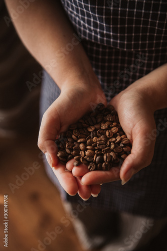 Woman's hands holding coffee beans. The woman is wearing a navy pinafore. Brown background.
