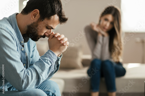 Young man feeling sad after arguing with his girlfriend on sofa at home