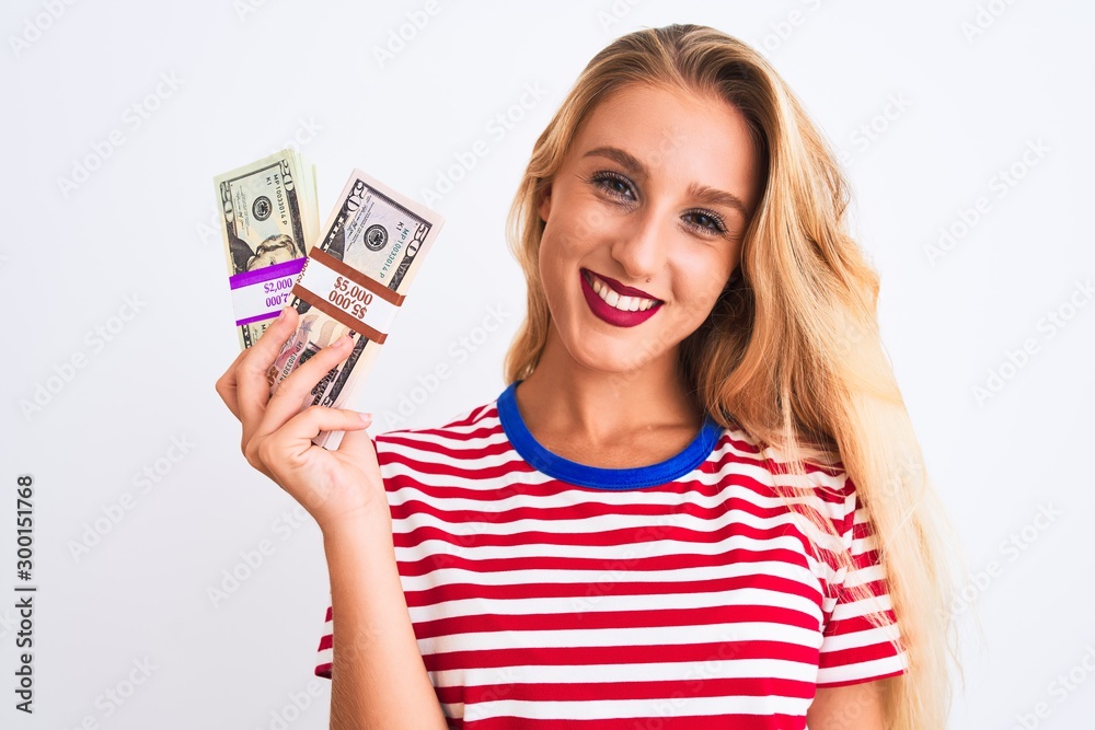 Beautiful woman wearing red striped t-shirt holding dollars over isolated white background with a happy face standing and smiling with a confident smile showing teeth Beautiful woman wearing red striped t-shirt holding dollars over isolated white background with a happy face standing and smiling with a confident smile showing teeth