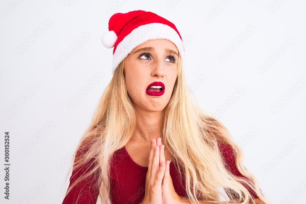 Young beautiful woman wearing Christmas Santa hat over isolated white background begging and praying with hands together with hope expression on face very emotional and worried. Asking Young beautiful woman wearing Christmas Santa hat over isolated white background begging and praying with hands together with hope expression on face very emotional and worried. Asking