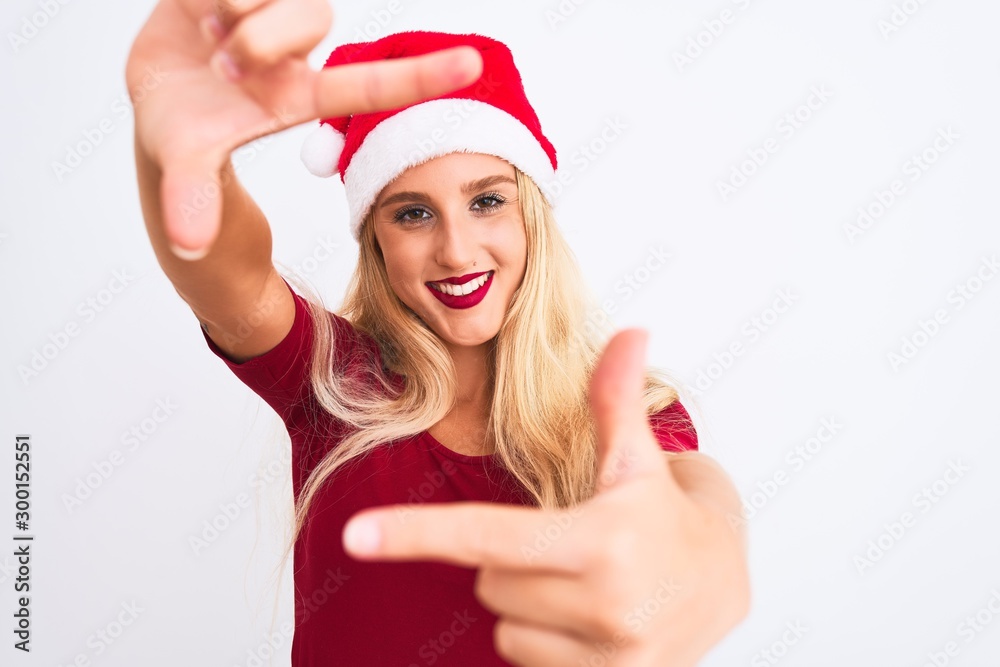 Young beautiful woman wearing Christmas Santa hat over isolated white background smiling making frame with hands and fingers with happy face. Creativity and photography concept. Young beautiful woman wearing Christmas Santa hat over isolated white background smiling making frame with hands and fingers with happy face. Creativity and photography concept.