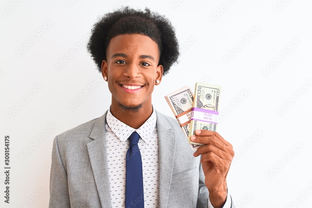 Young african american businessman holding dollars standing over isolated white background with a happy face standing and smiling with a confident smile showing teeth Young african american businessman holding dollars standing over isolated white background with a happy face standing and smiling with a confident smile showing teeth
