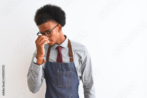 Young african american shopkeeper man wearing apron glasses over isolated white background tired rubbing nose and eyes feeling fatigue and headache. Stress and frustration concept.