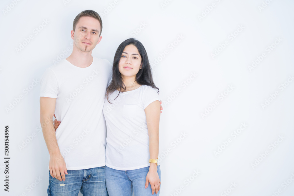 Young beautiful couple wearing casual t-shirt standing over isolated white background with serious expression on face. Simple and natural looking at the camera. Young beautiful couple wearing casual t-shirt standing over isolated white background with serious expression on face. Simple and natural looking at the camera.