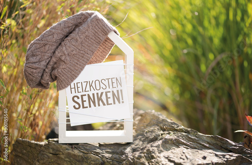 Weißes Haus im Garten mit Schild Heizkosten senken!
