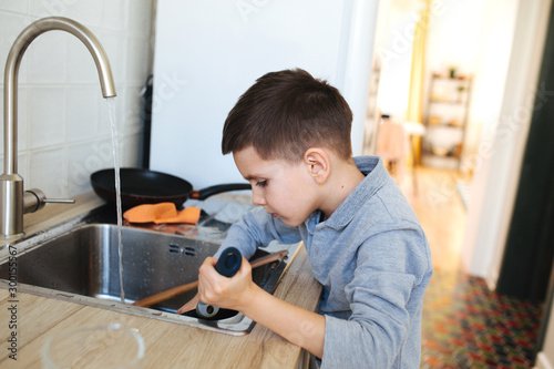 Obraz na plátně Little boy washing dishes in the kitchen at home