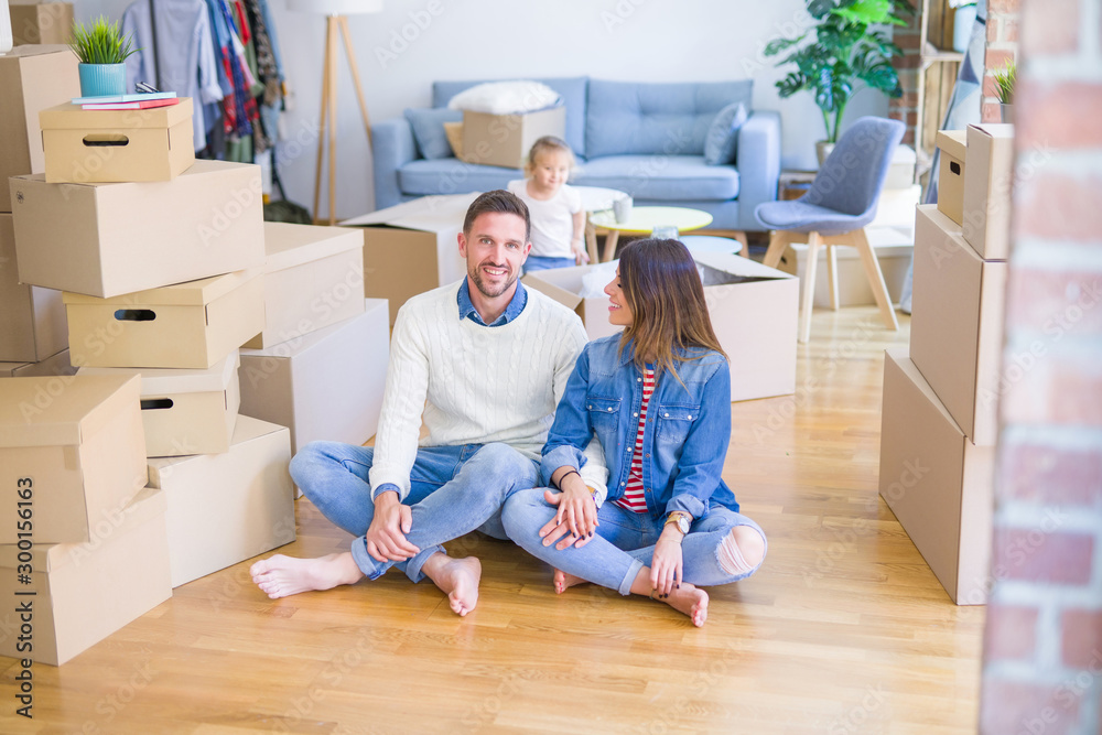Beautiful family sitting on the floor playing with his kid at new home around cardboard boxes Beautiful family sitting on the floor playing with his kid at new home around cardboard boxes