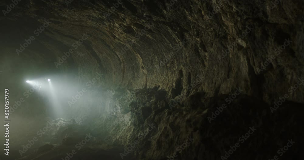 Tracking shot of explorers hiking through smoky cave towards camera