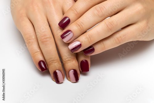 Hands close up. Burgundy beige manicure with a pink shiny strip on short square nails. Half a manicure. Color manicure.