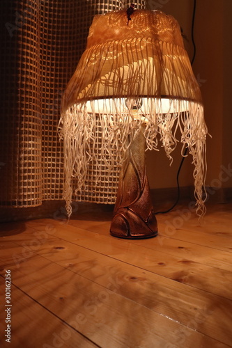 a lamp with a lampshade stands on a wooden surface casts bizarre shadows and illuminates the whole space with a warm golden light