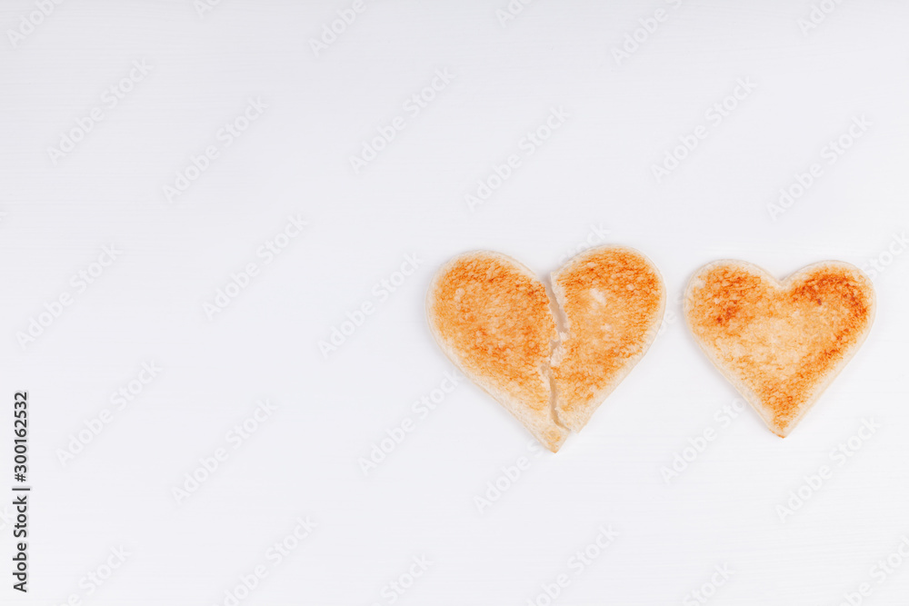 Fototapeta premium Bread toast broken heart with whole heart together on white background. The concept of divorce, breakup, unhappy relationship. Copy space.