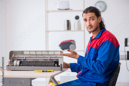 Young male contractor repairing air-conditioner at workshop