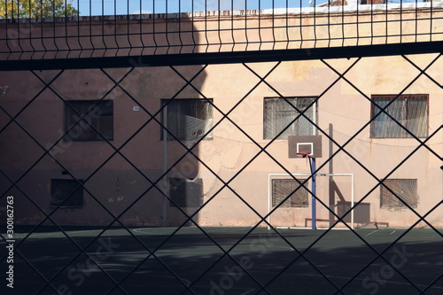 View through a fence on a basketball hoop lit by the autumn sun on an empty playground