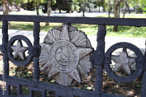 The fence of the park with a sickle and hammer sign, a Soviet star, a bayonet and a sword. The inscription 