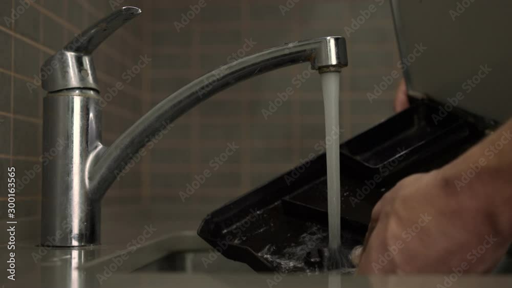 man washes black plastic coffee machine removable drip tray under tap water using yellow sponge close view man washes black plastic coffee machine removable drip tray under tap water using yellow sponge close view