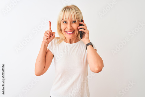 Middle age woman talking on the smartphone standing over isolated white background surprised with an idea or question pointing finger with happy face, number one
