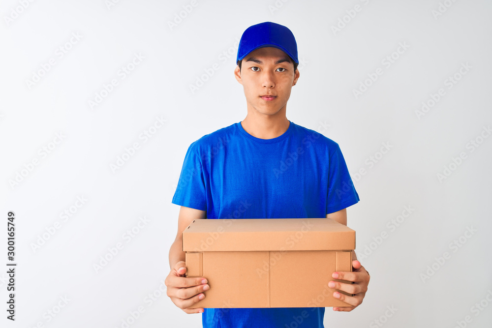 Chinese deliveryman wearing cap holding box standing over isolated white background with a confident expression on smart face thinking serious Chinese deliveryman wearing cap holding box standing over isolated white background with a confident expression on smart face thinking serious