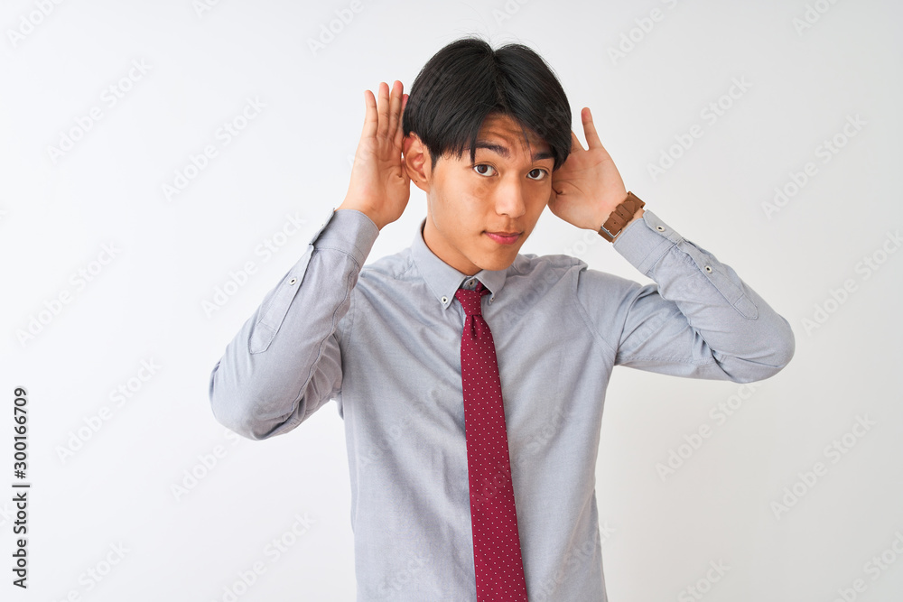 Chinese businessman wearing elegant tie standing over isolated white background Trying to hear both hands on ear gesture, curious for gossip. Hearing problem, deaf Chinese businessman wearing elegant tie standing over isolated white background Trying to hear both hands on ear gesture, curious for gossip. Hearing problem, deaf