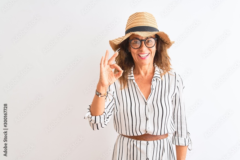 Middle age businesswoman wearing striped dress glasses hat over isolated white background doing ok sign with fingers, excellent symbol Middle age businesswoman wearing striped dress glasses hat over isolated white background doing ok sign with fingers, excellent symbol