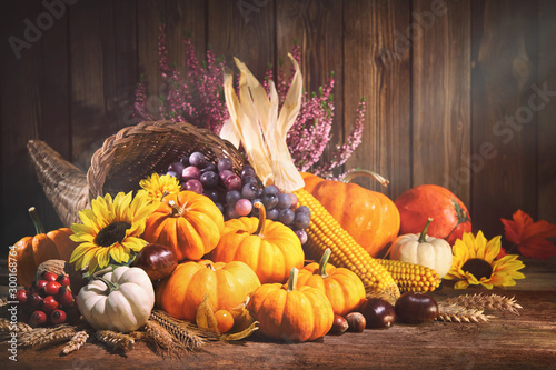 Pumpkins with fruits and falling leaves on rustic wooden table photo