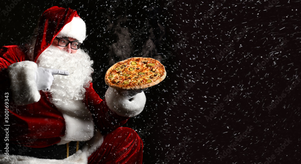 Happy laughing Santa Claus hold big hot steaming original pizza offering pointing finger. New year and Xmas fast food - obrazy, fototapety, plakaty 