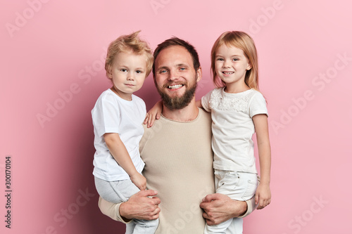 cheerful smiling daddy holding his kids in arms, parenthood, free time, spare time, close up portrait, isolated pink background, studio shot