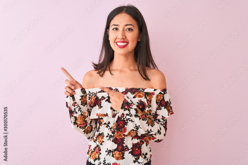Young chinese woman wearing floral t-shirt standing over isolated pink background smiling and looking at the camera pointing with two hands and fingers to the side. Young chinese woman wearing floral t-shirt standing over isolated pink background smiling and looking at the camera pointing with two hands and fingers to the side.
