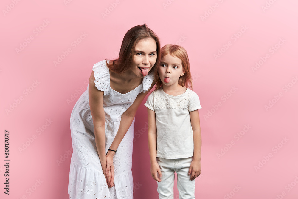 Close up portrait of careless pretty joyful funny mother and her daughter showing tongue, close eup portrait, isolated pink background, facial expression, reaction Close up portrait of careless pretty joyful funny mother and her daughter showing tongue, close eup portrait, isolated pink background, facial expression, reaction